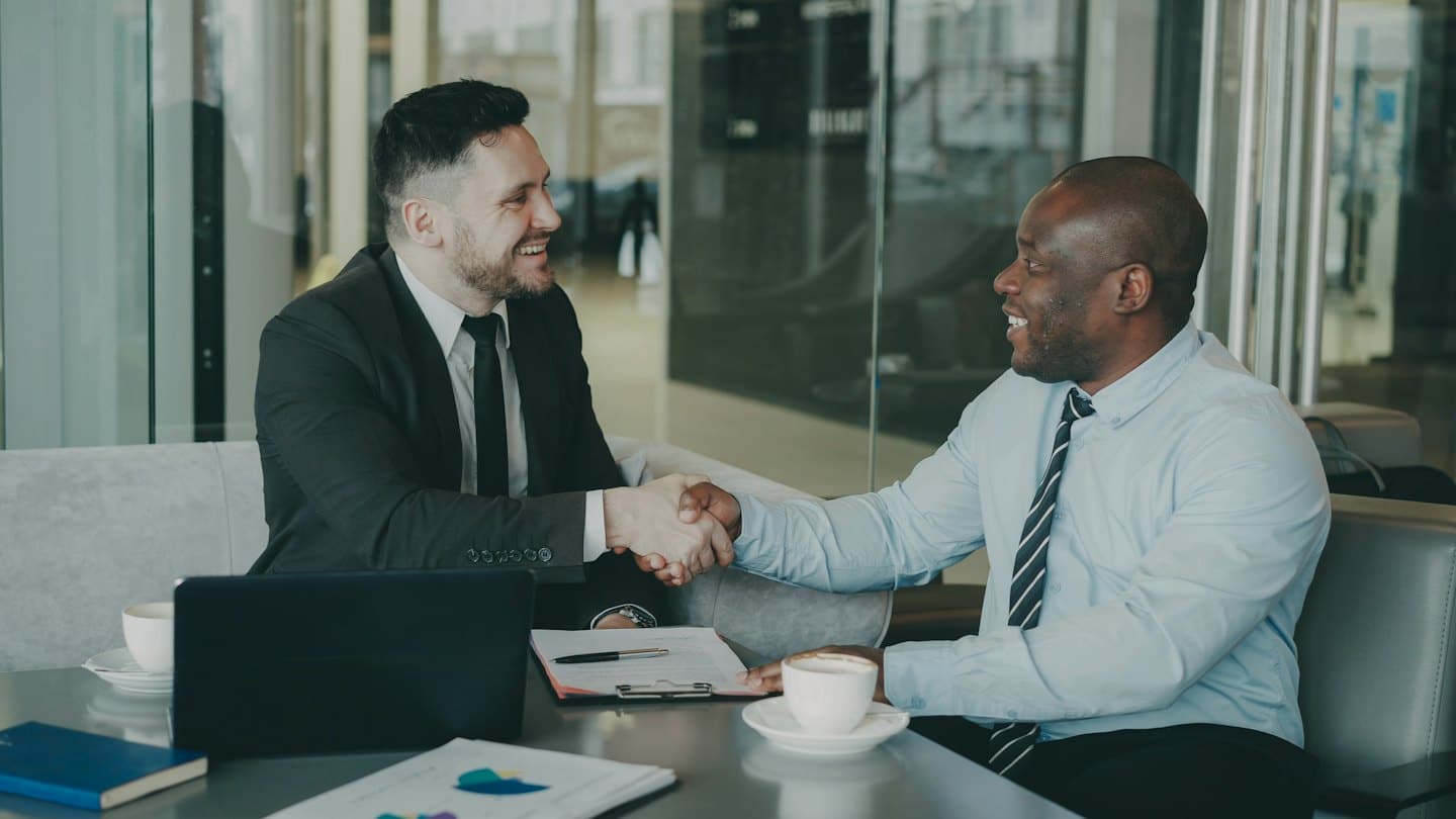 Two business professionals shake hands over a conference table.